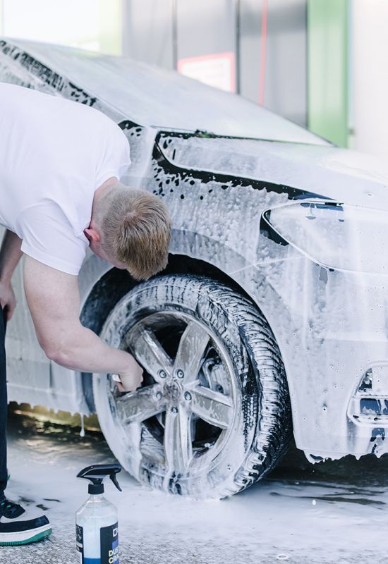 Mann reinigt Autoreifen während Schaumpflege bei professioneller Außenreinigung eines VW-Fahrzeugs