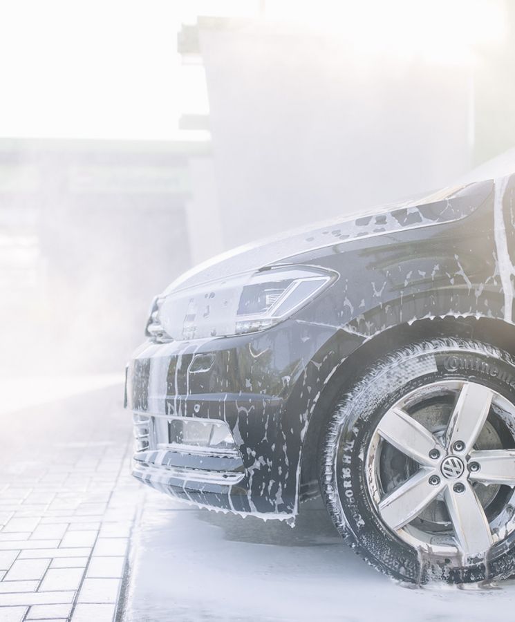 Vorderansicht eines eingeschäumten VW bei der Außenwäsche – Fahrzeugpflege mit Schaumreiniger im Sonnenlicht