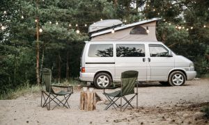 Campingbus mit Dachzelt im Wald bei Lichterketten – gemütlicher Outdoor-Stellplatz mit zwei Campingstühlen im Sand
