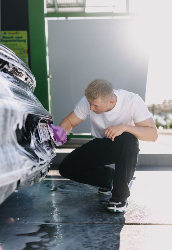 Mitarbeiter reinigt Autokennzeichen gründlich mit Handschuh bei professioneller Fahrzeugwäsche