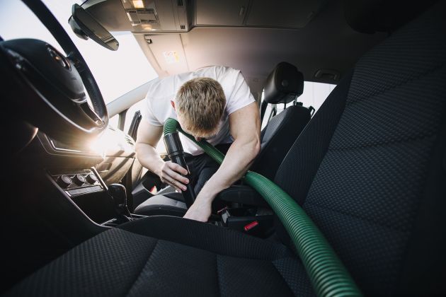 Fahrzeuginnenreinigung mit Staubsauger – Autopfleger saugt gründlich den Innenraum bei der professionellen Aufbereitung